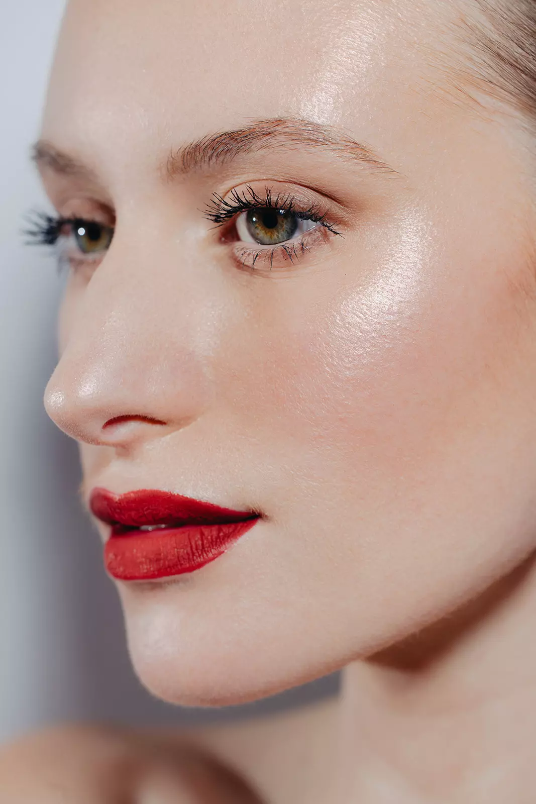 Close up portrait emphasizing radiant skin texture and refined red lip makeup