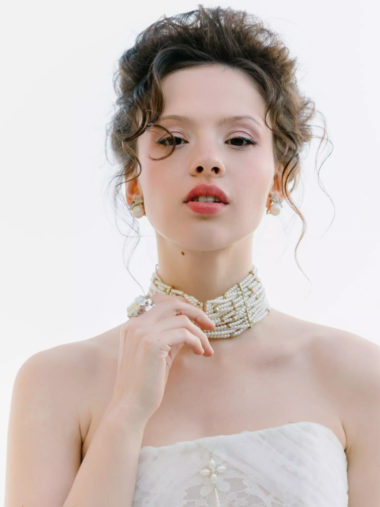 Bride adjusting pearl necklace showcasing luminous skin and precise bridal makeup by Mandy Dorian