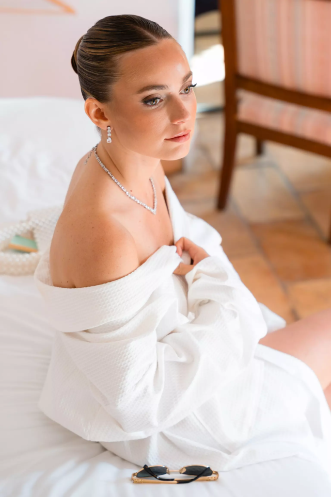 Bride seated indoors featuring refined makeup and structured bridal hairstyle aligned with couture gown