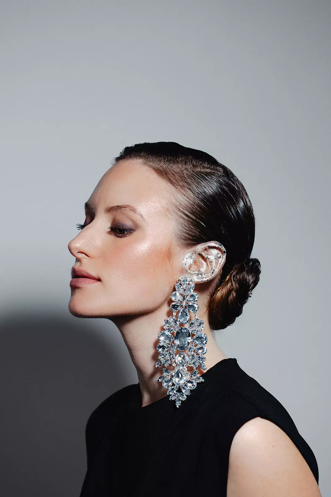 Model wearing oversized crystal earrings with luminous makeup and sleek hairstyle