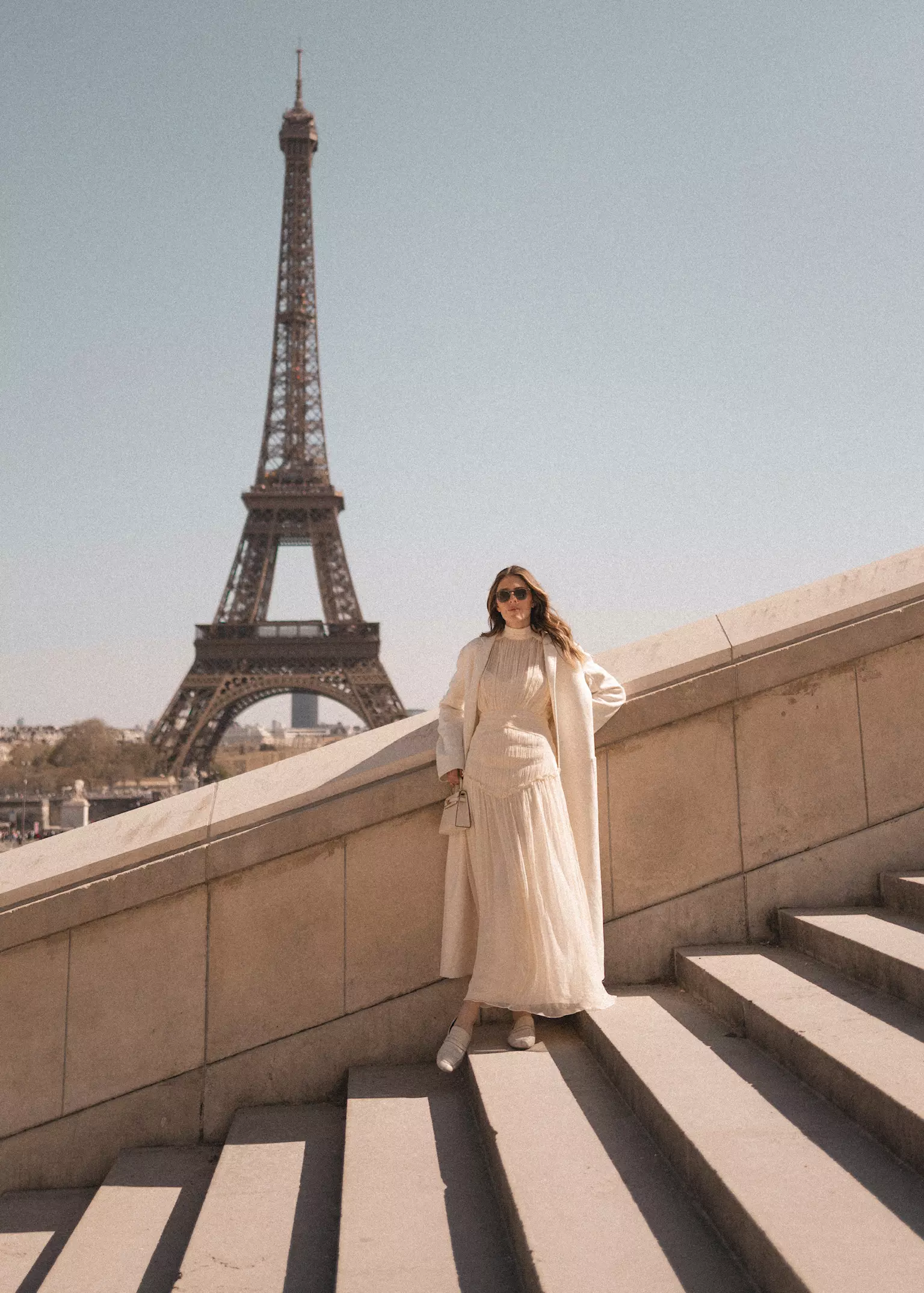 Bride standing near Eiffel Tower in elegant dress with soft bridal waves and luminous complexion