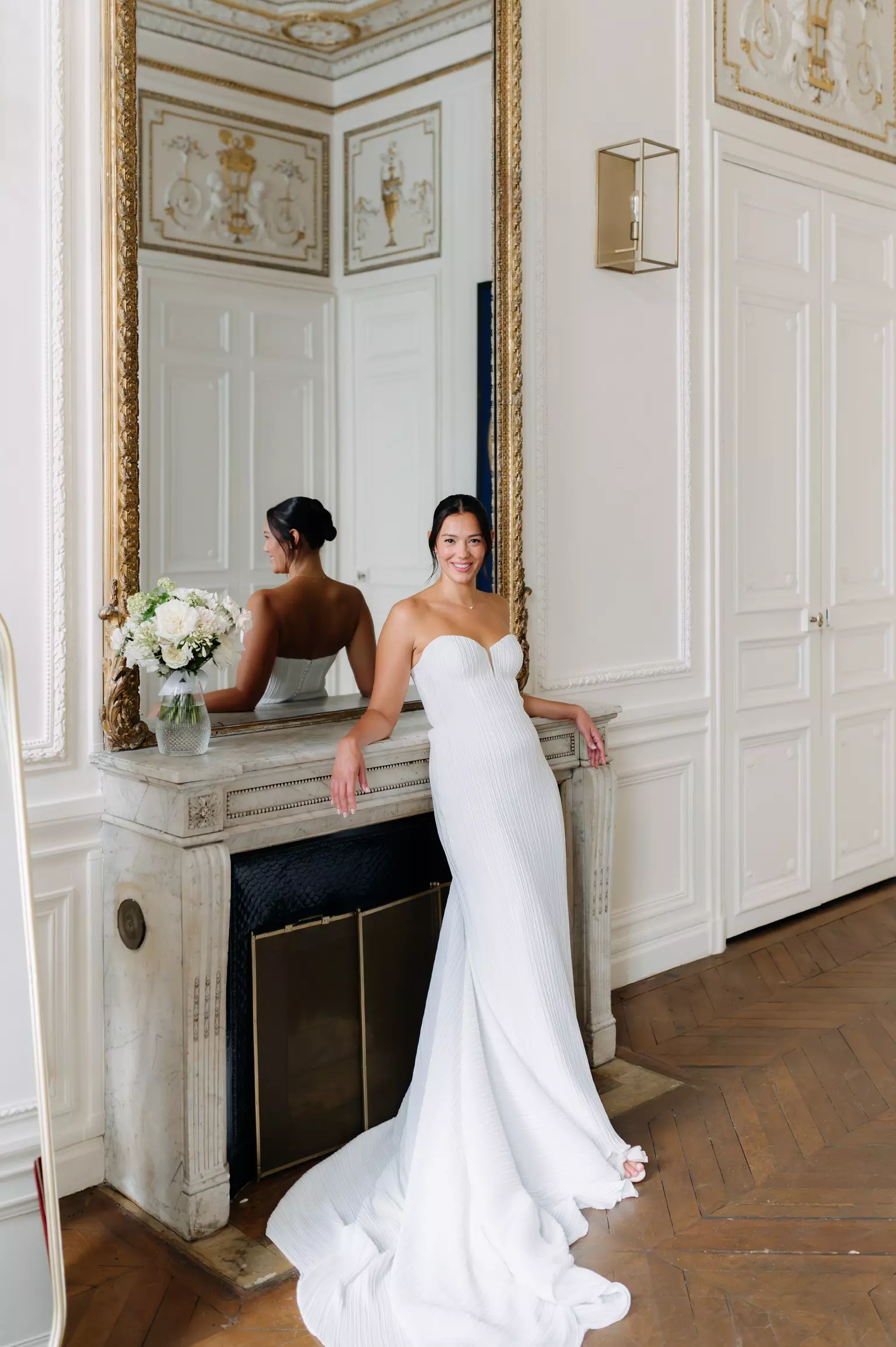 Bride Erin standing by mirror with sleek low bun hairstyle and luminous bridal makeup by Mandy Dorian in Paris