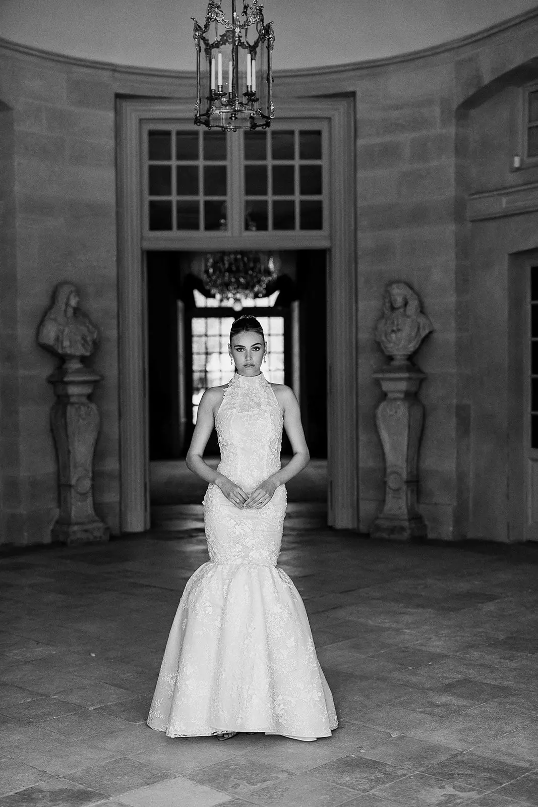 Bride standing in grand château hall featuring refined bridal hair and luminous makeup styling