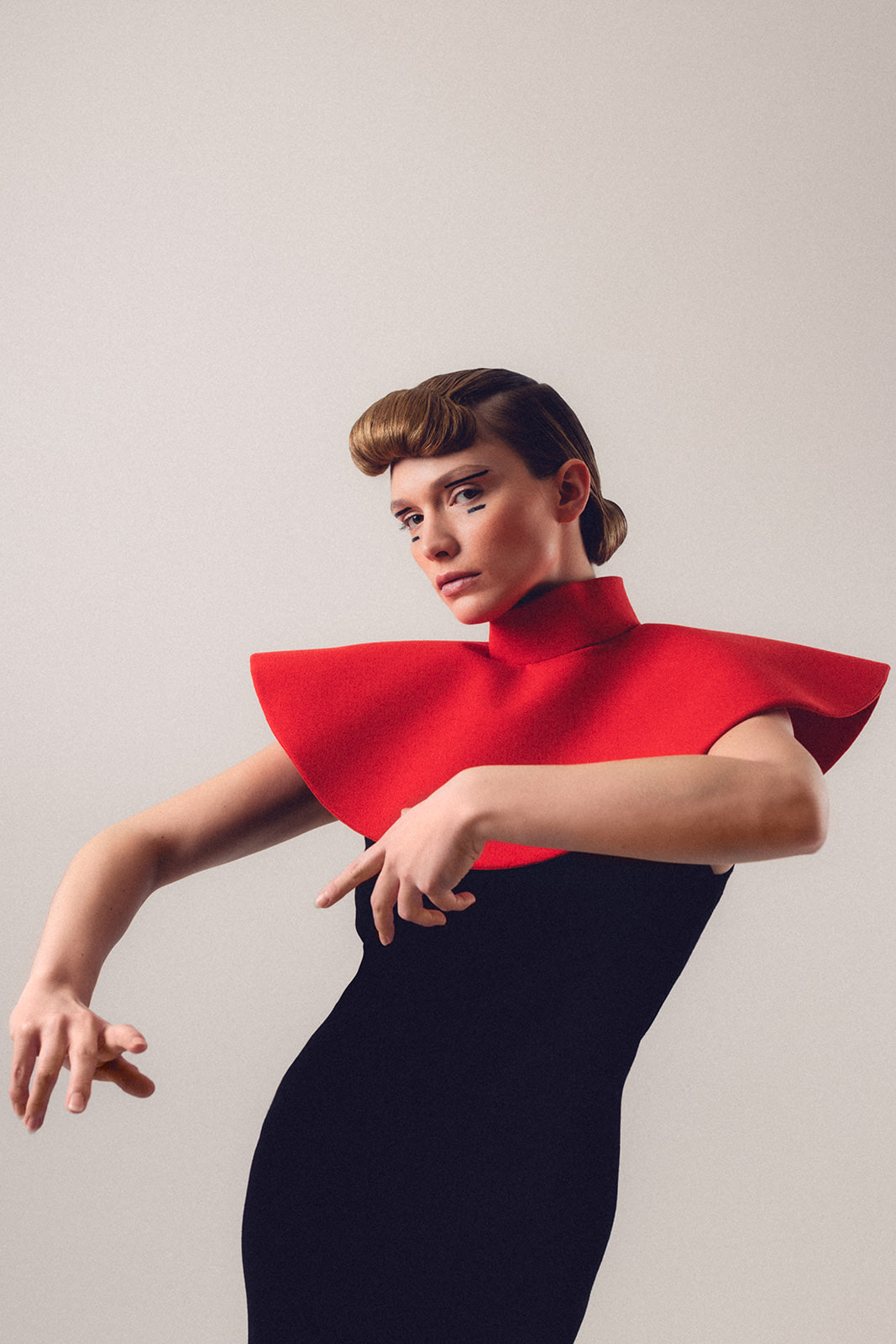 Model wearing dramatic red collar dress with sharp editorial makeup and structured hair styling