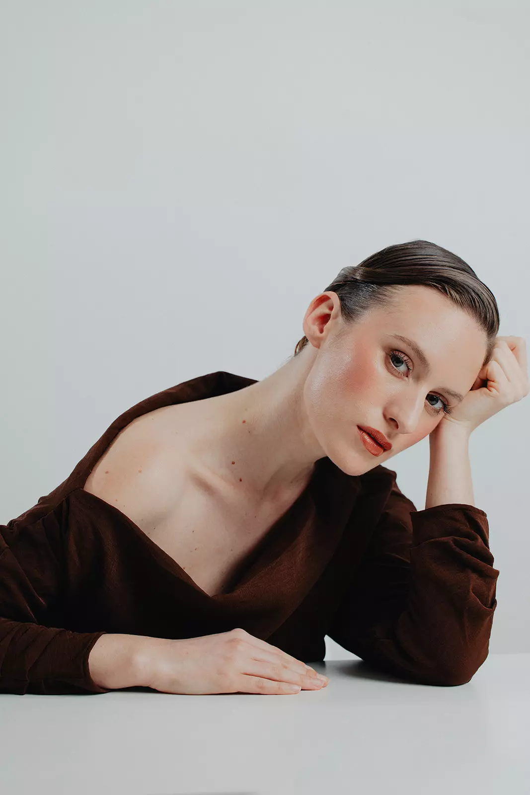 Model resting head on hand featuring soft sculpted contour and sleek low bun hairstyle