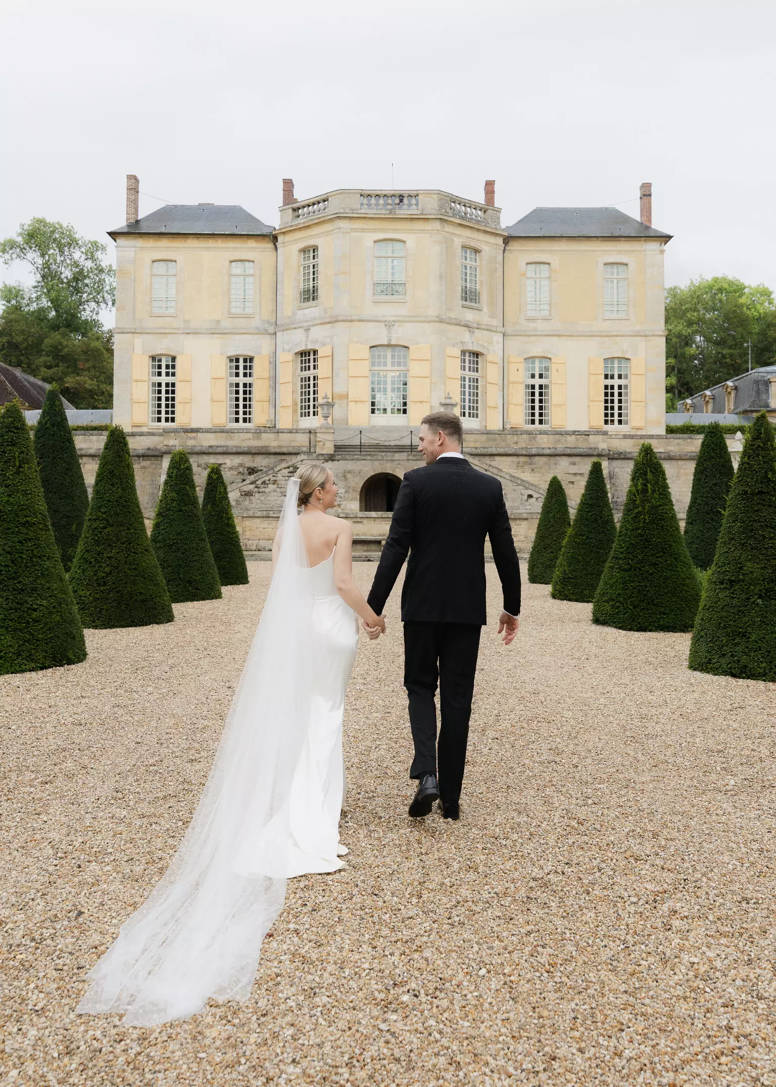 Bride and groom walking toward Château de Villette featuring elegant bridal hair and makeup styling by Mandy Dorian