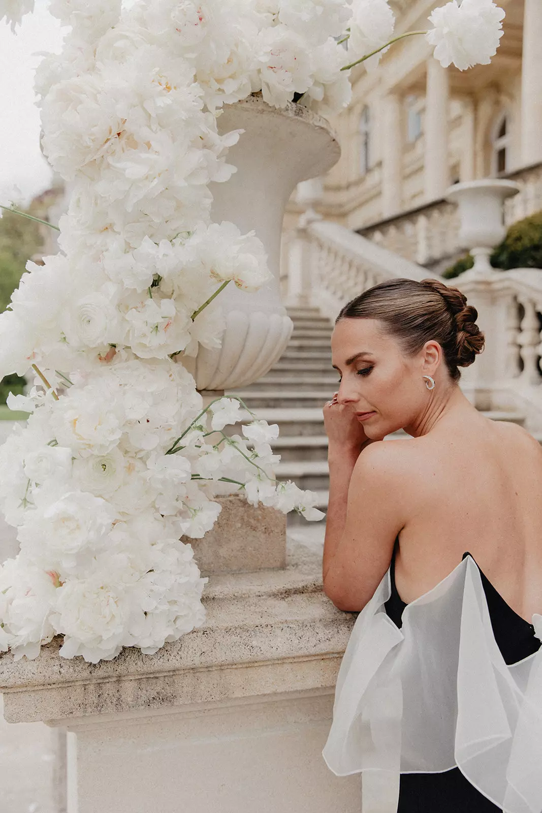 Bride Laura beside white floral arrangement showcasing intentional bridal makeup and smooth low bun hairstyle