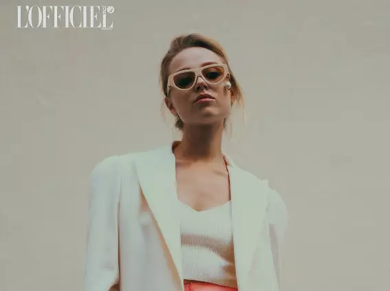Model wearing white blazer and sunglasses with polished editorial makeup and modern hairstyling