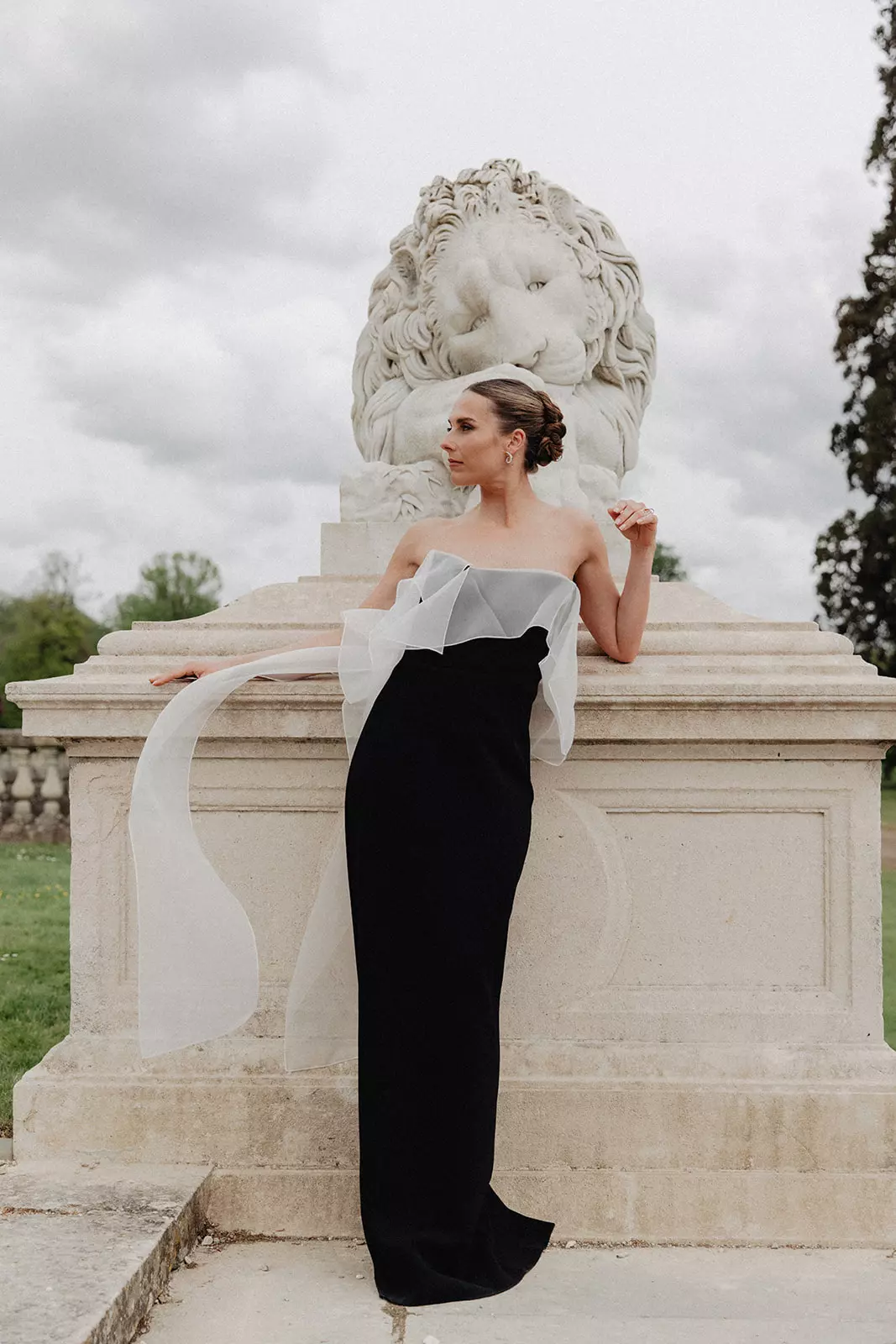 Bride in sculptural black and white gown with polished bridal hair and makeup in front of château statue