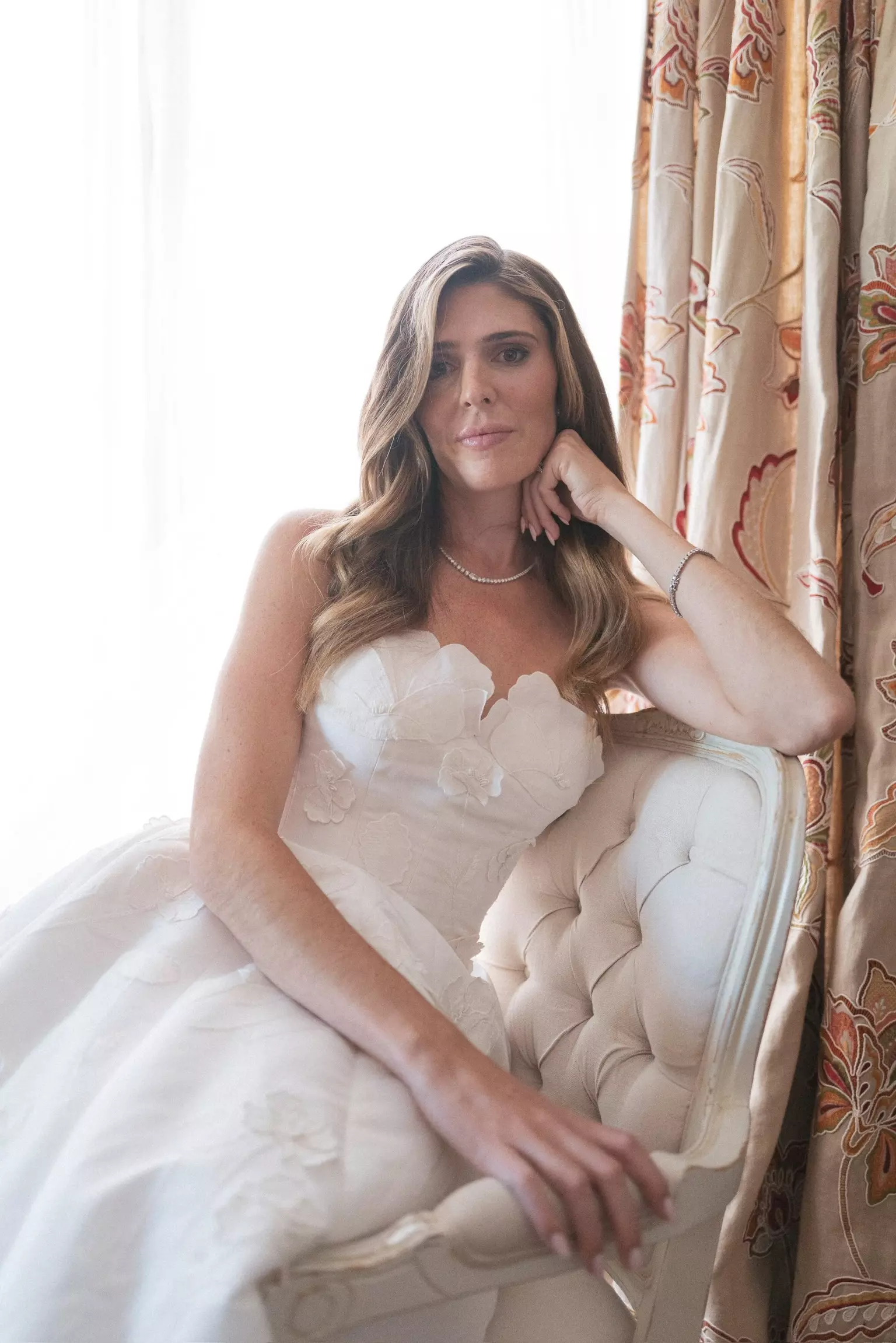 Bride seated indoors featuring soft waves and luminous complexion designed for multi-day wedding celebration