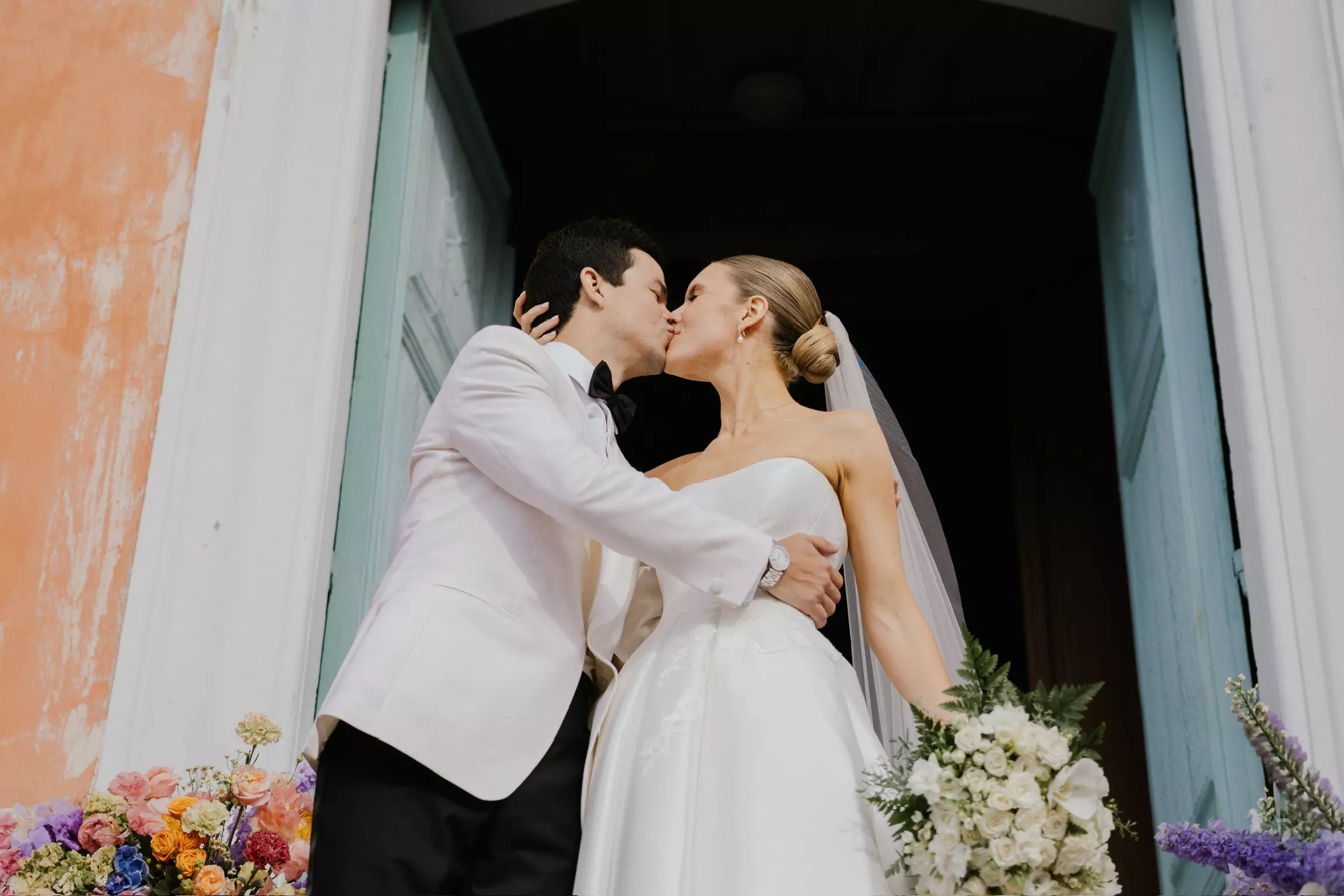 Bride and groom kissing after church ceremony with elegant bridal bun and luminous makeup styling