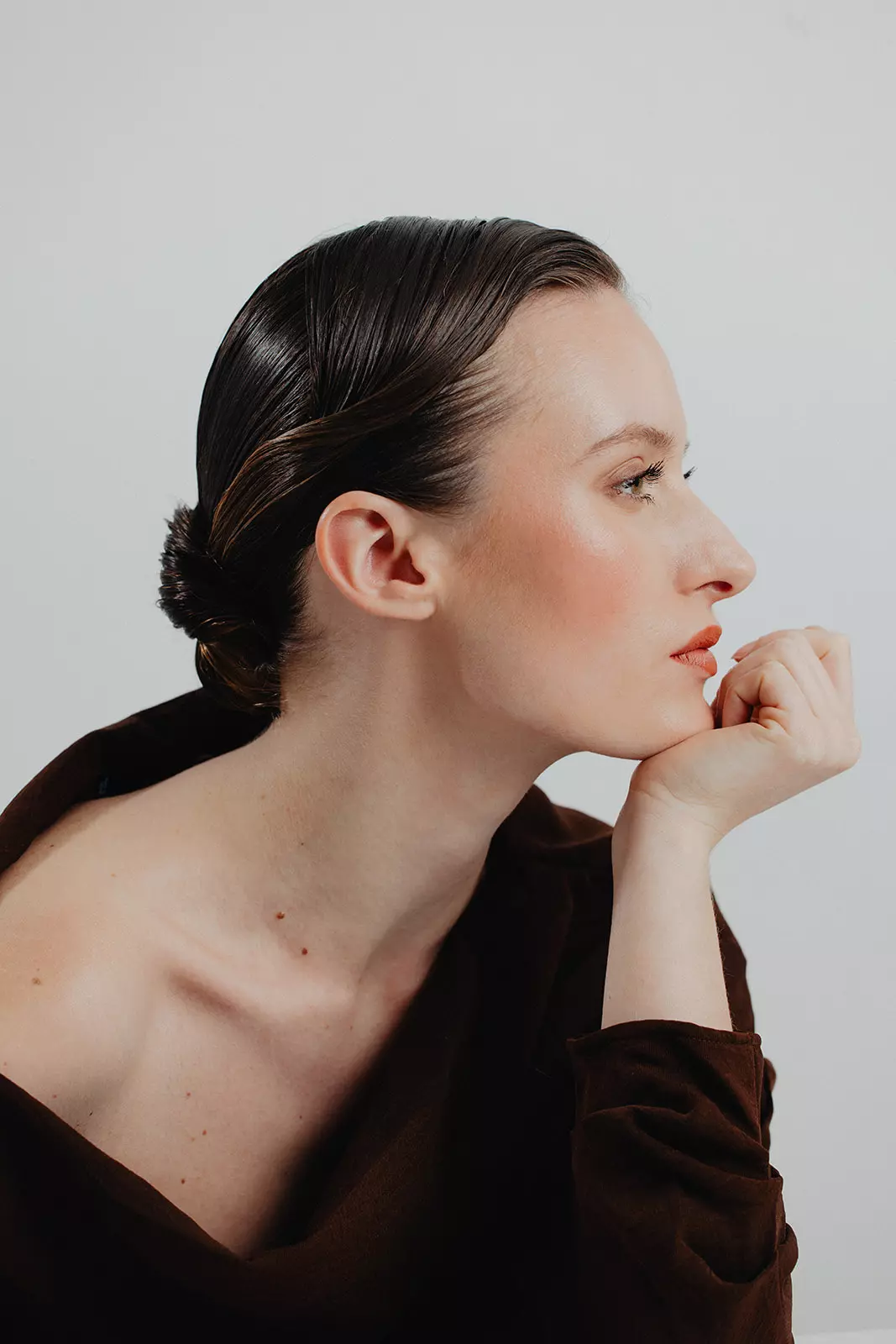 Model in side profile with sleek low bun and luminous sculpted makeup by Mandy Dorian