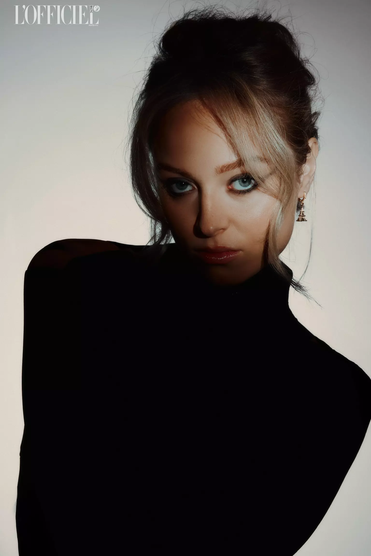 Model in black outfit with dramatic lighting highlighting bold fashion makeup and structured hairstyle