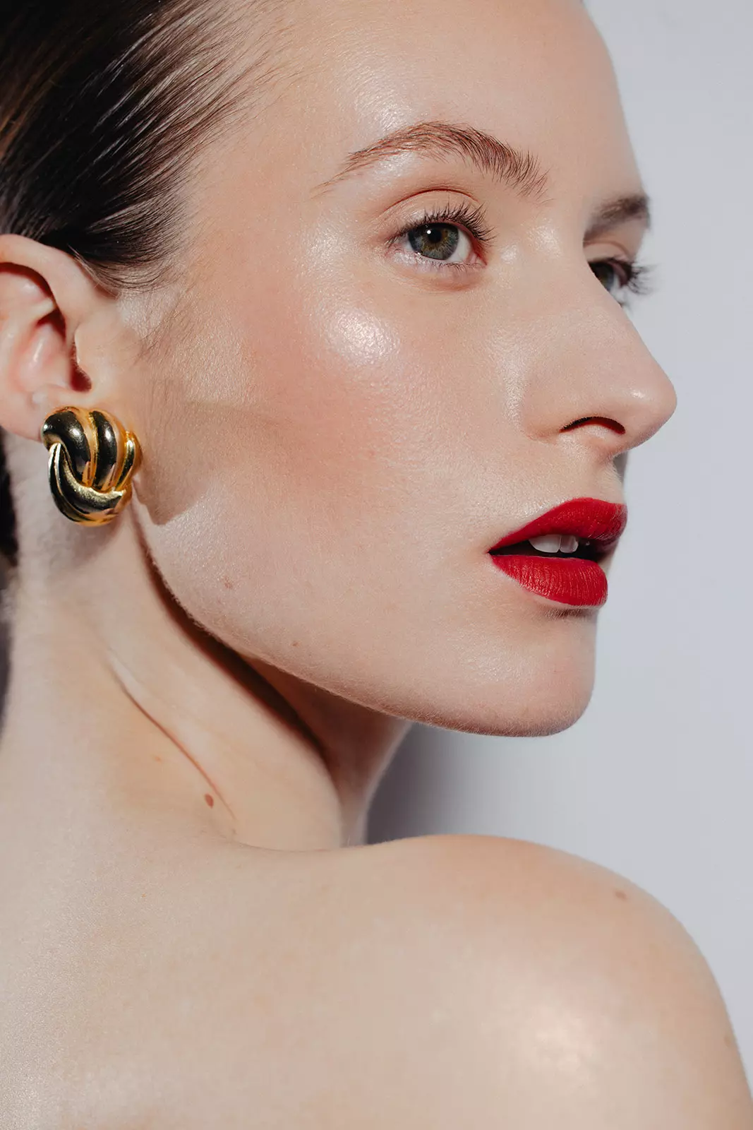 Close portrait highlighting defined eye makeup and statement red lip with sculpted glow