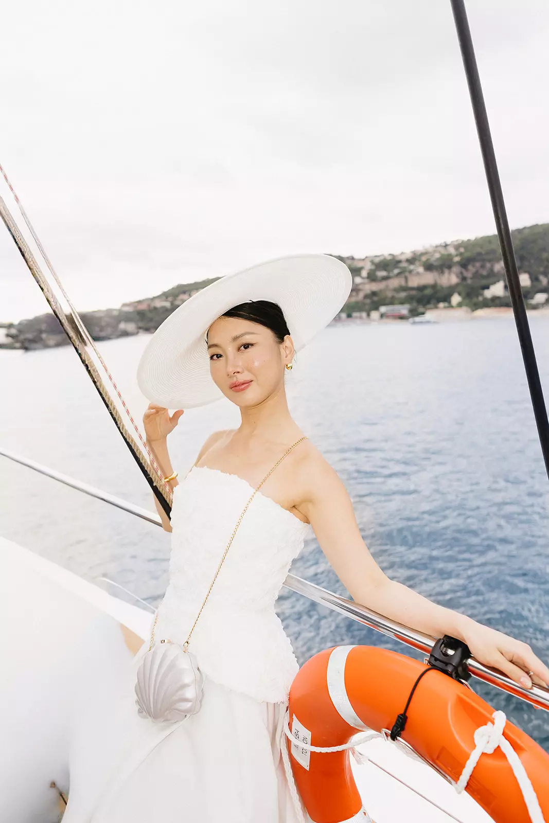 Bride wearing wide hat on yacht with elegant minimal makeup and structured bridal bun