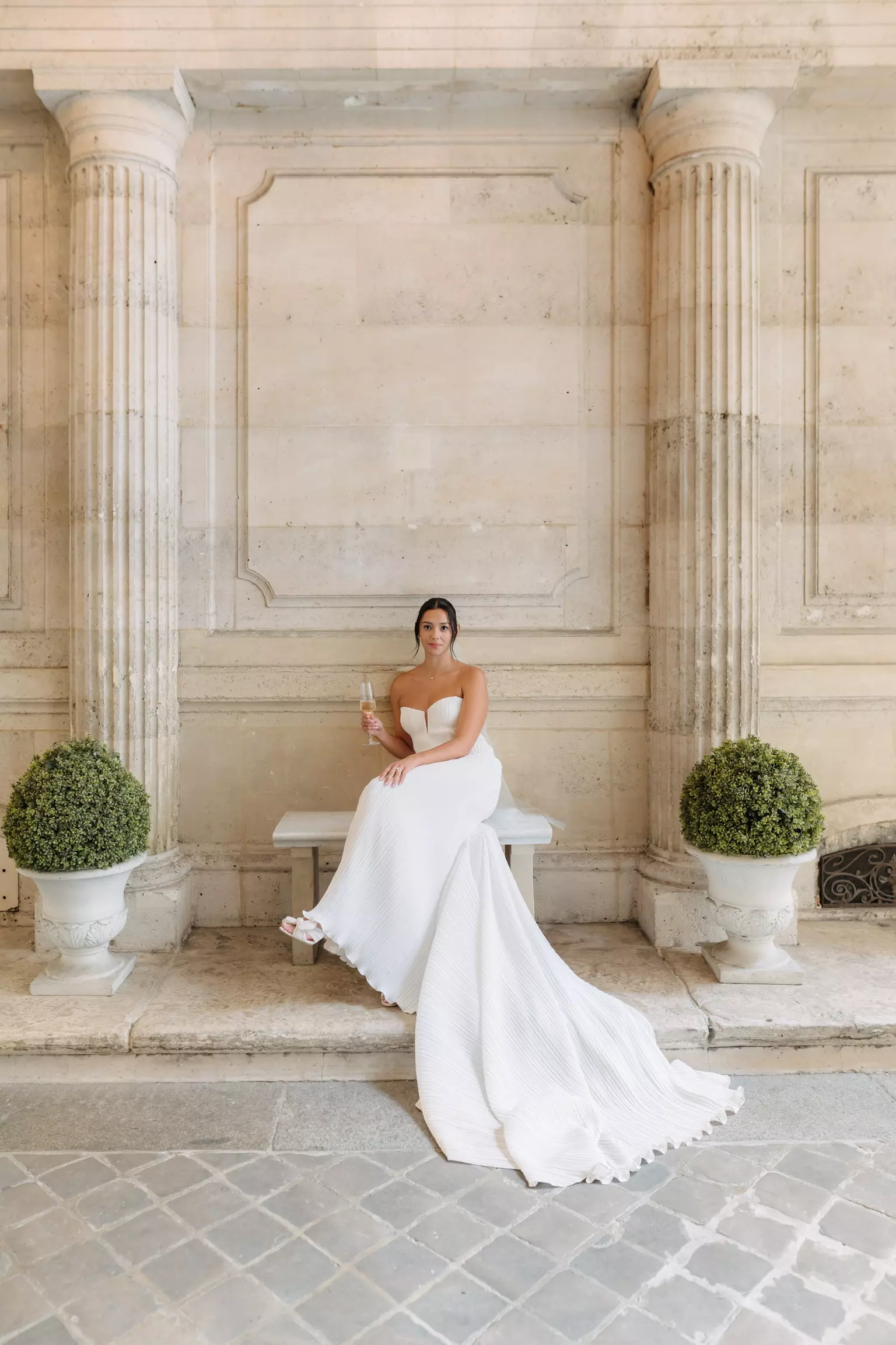 Bride seated outside Hôtel Alfred Sommier wearing structured gown with polished bridal hair and makeup