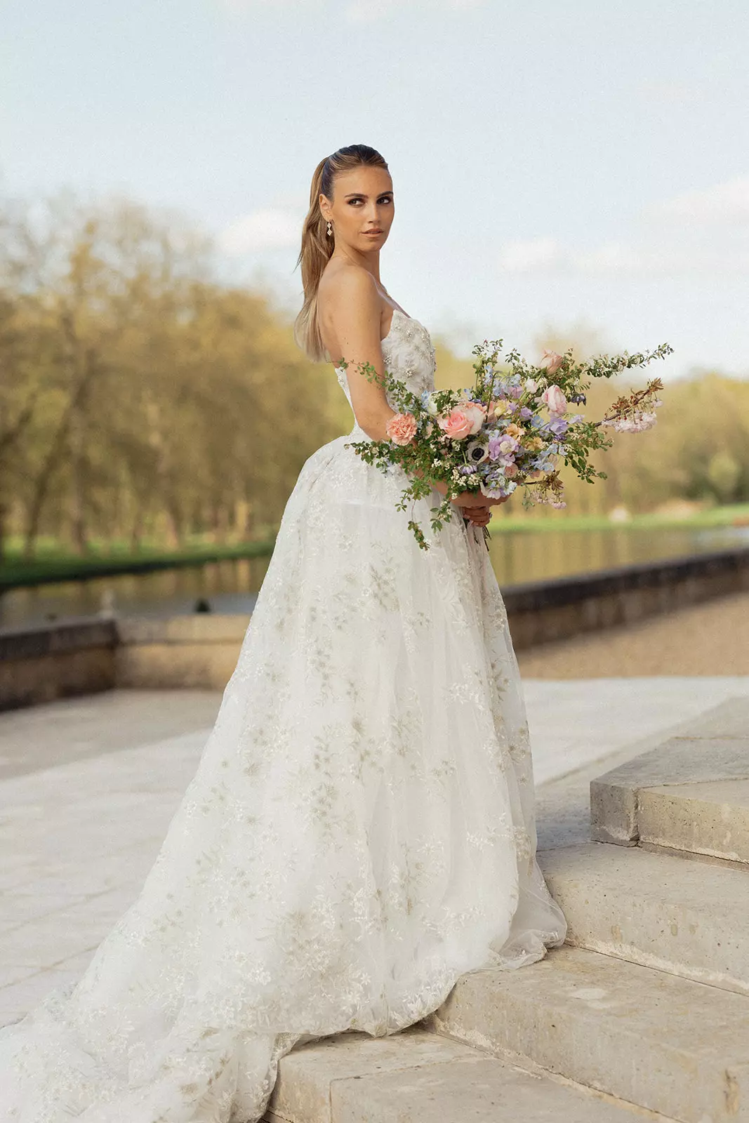 Bride holding bouquet at Château de Villette wearing romantic bridal hairstyle and natural radiant makeup