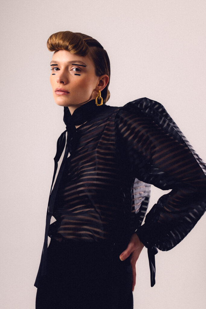 Model in black textured outfit featuring bold editorial makeup and sculpted hair design