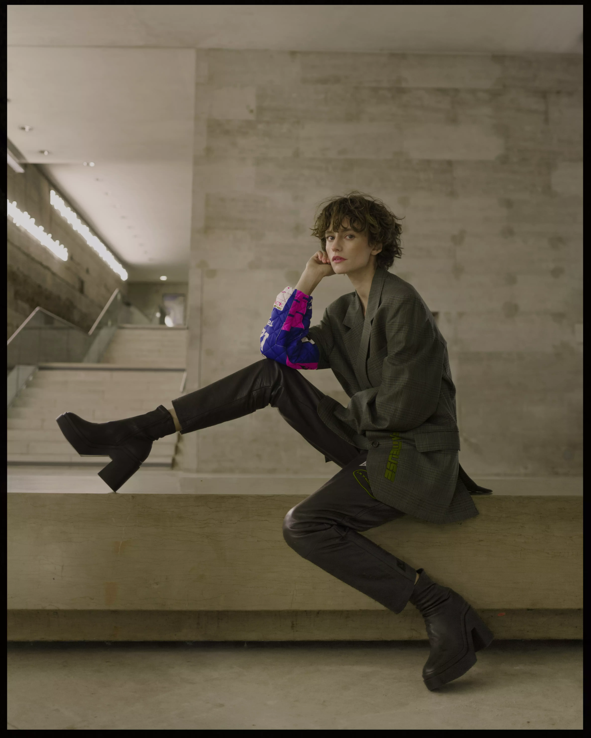 Model seated on stairs wearing structured outfit with polished hair and defined makeup look